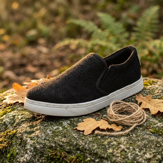 Black pure hemp slip-on shoe with white rubber sole on a rock with leaves and twine