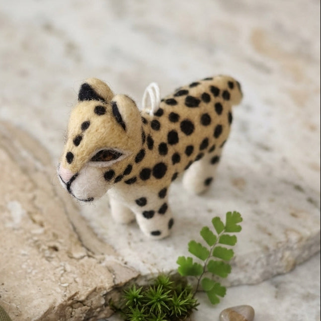Handmade leopard felt ornament with spotted details standing on a stone surface with greenery