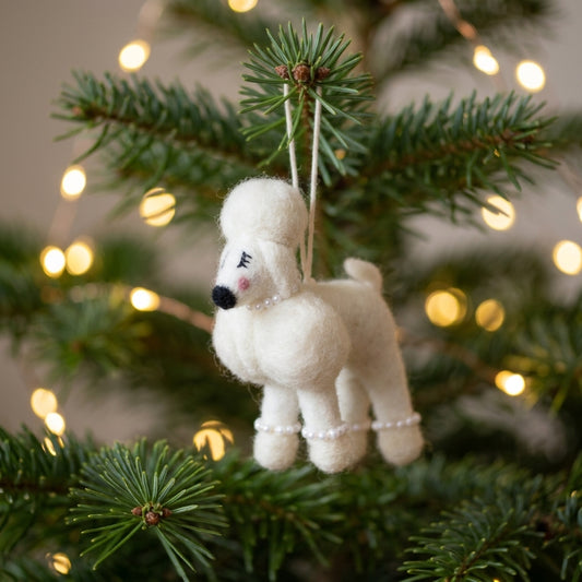 Handmade wool felt poodle dog ornament t hanging on a Christmas tree with lights in the background