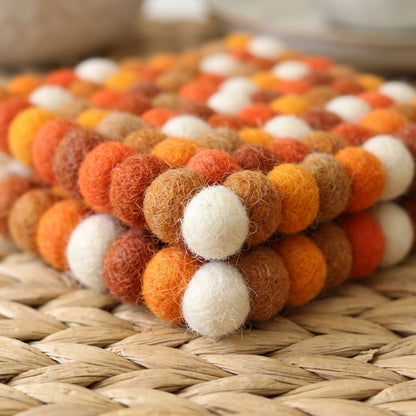 Stack of felted balls in orange, brown, and white on a woven surface