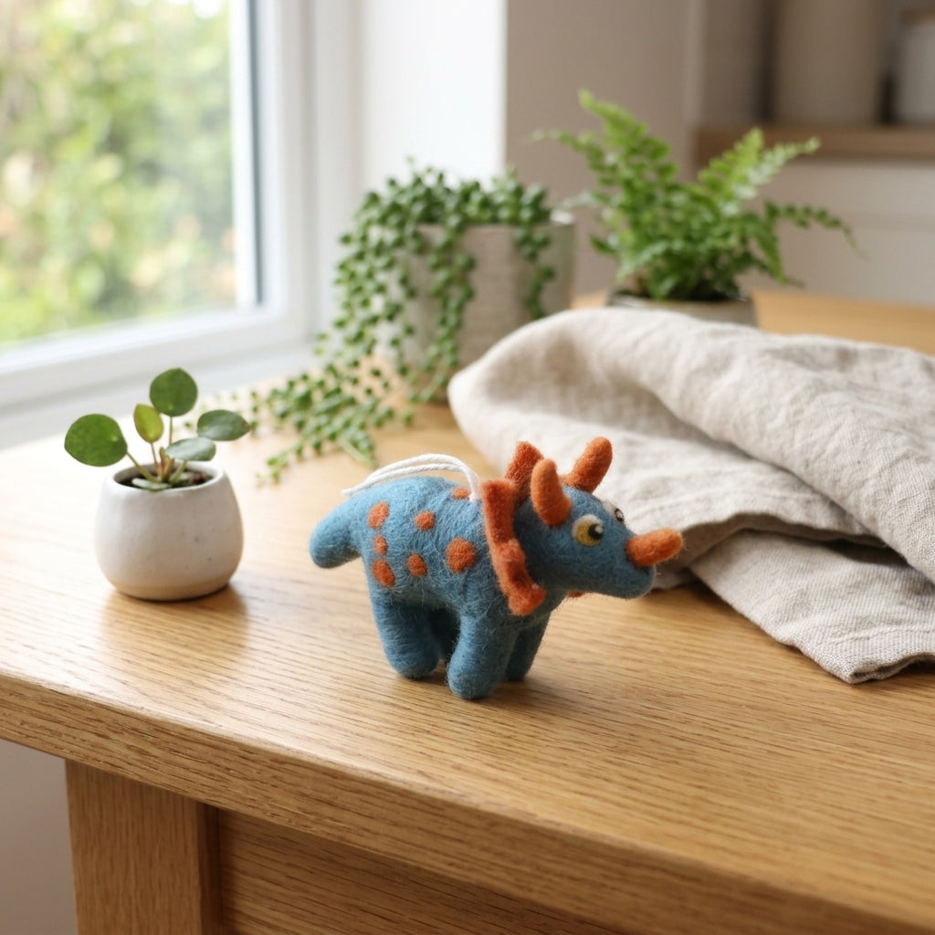 Triceratops wool felt ornament with handmade horn details on a wooden surface with plants in the background