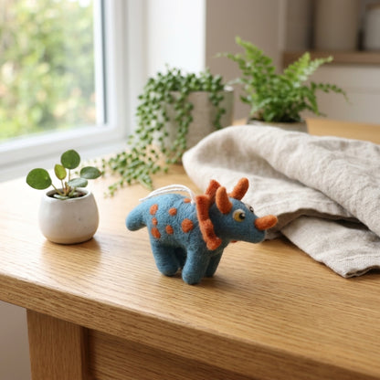 Triceratops wool felt ornament with handmade horn details on a wooden surface with plants in the background