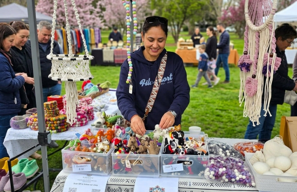 Woman at an outdoor market stall selling various items, with a 'Namaste' sign visible.