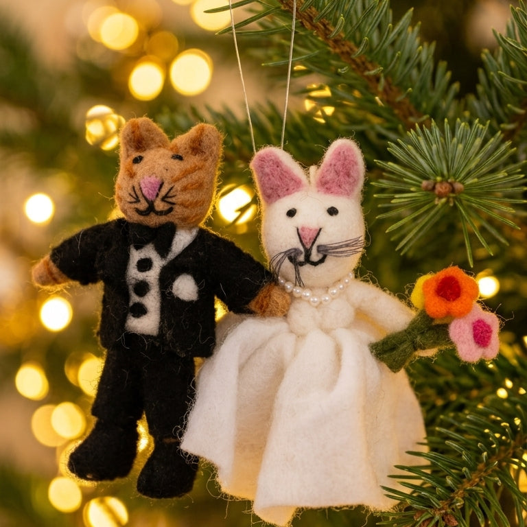 Wool felt cat bride and groom ornament hanging on a Christmas tree with lights in the background.