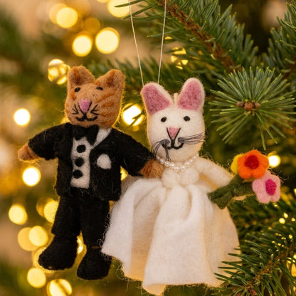 Wool felt cat bride and groom ornament hanging on a Christmas tree with lights in the background.