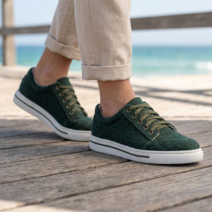 Person wearing dark green textured organic hemp canvas lace-up shoes with white natural rubber soles on a wooden boardwalk by the ocean.