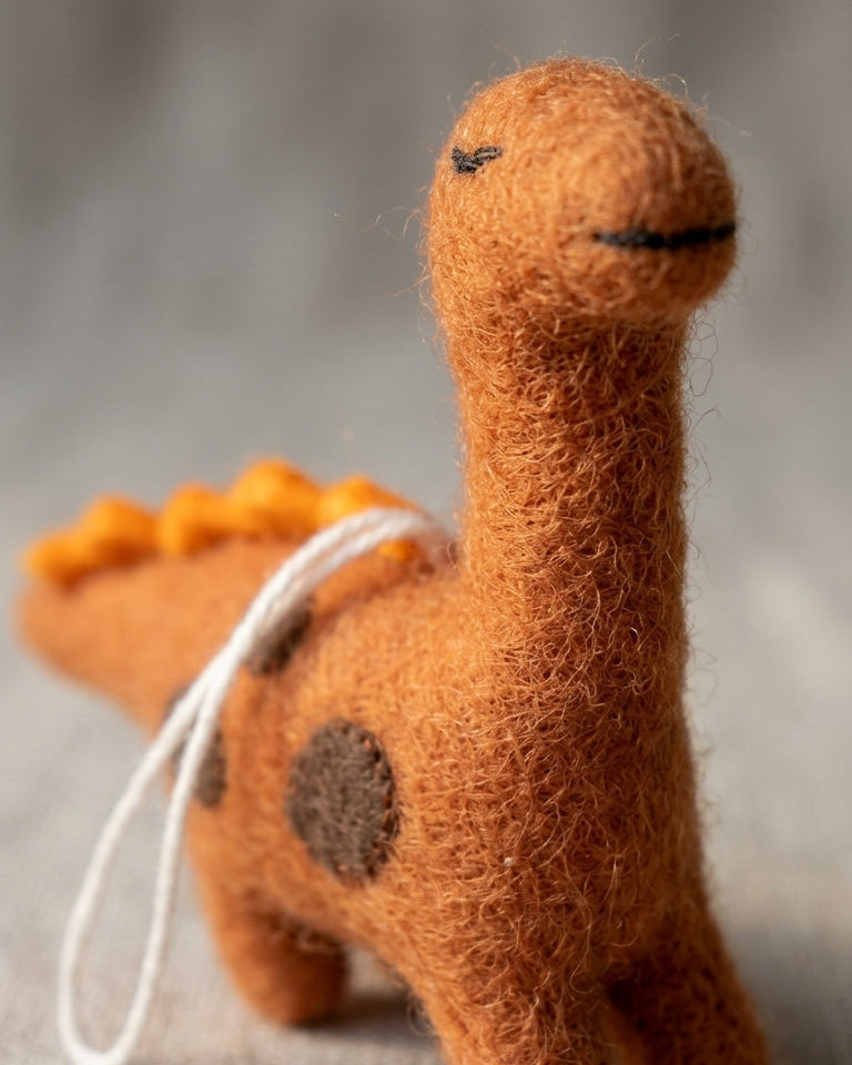 Handmade stegosaurus felt ornament with orange spines with a white string on a textured surface