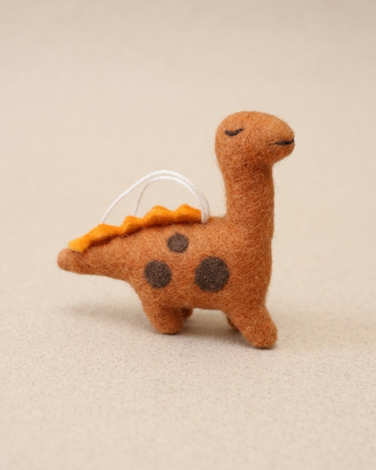 Handmade dinosaur felt ornament with spotted details on a beige background
