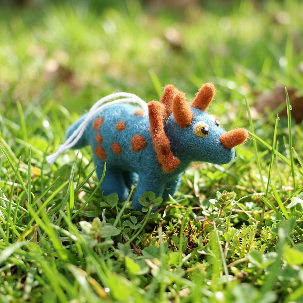Handmade wool felt triceratops ornament with hanging thread with orange spots and spikes on grass